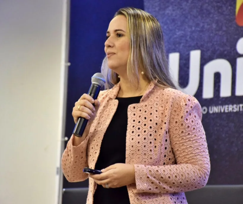 Cristiane Barreto apresentando no Congresso Internacional de Psicologia Social, microfone na mão, diante do banner da Universidad Kennedy em Buenos Aires