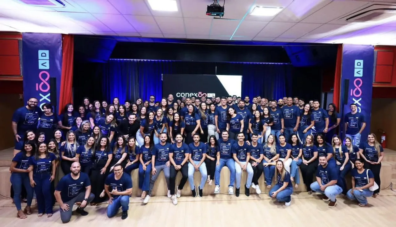 Cerca de cem profissionais da AD Promotora, de camisas azul-marinho iguais, reunidos no palco no encerramento do dia de treinamento corporativo Conexão AD