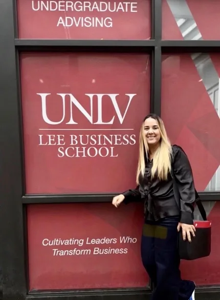 Cristiane Barreto em frente à UNLV Lee Business School, em Las Vegas, ao lado da sinalização vermelha da entrada